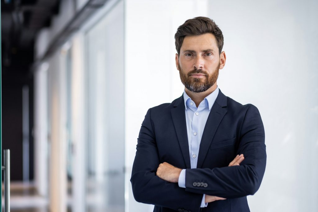 Portrait of serious self-confident male lawyer standing in office, crossed arms on chest and